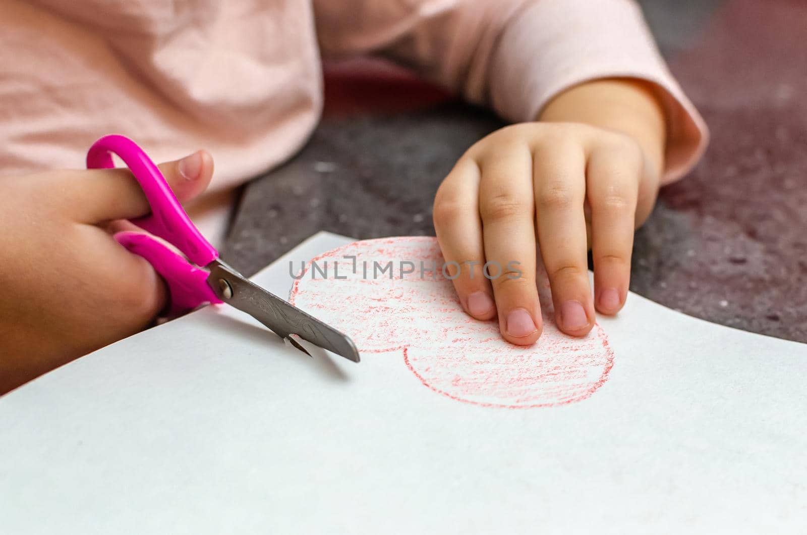 The girl's hand holds a heart cut from paper. Children's creativity - drawings and crafts for Valentine's Day or Mother's Day