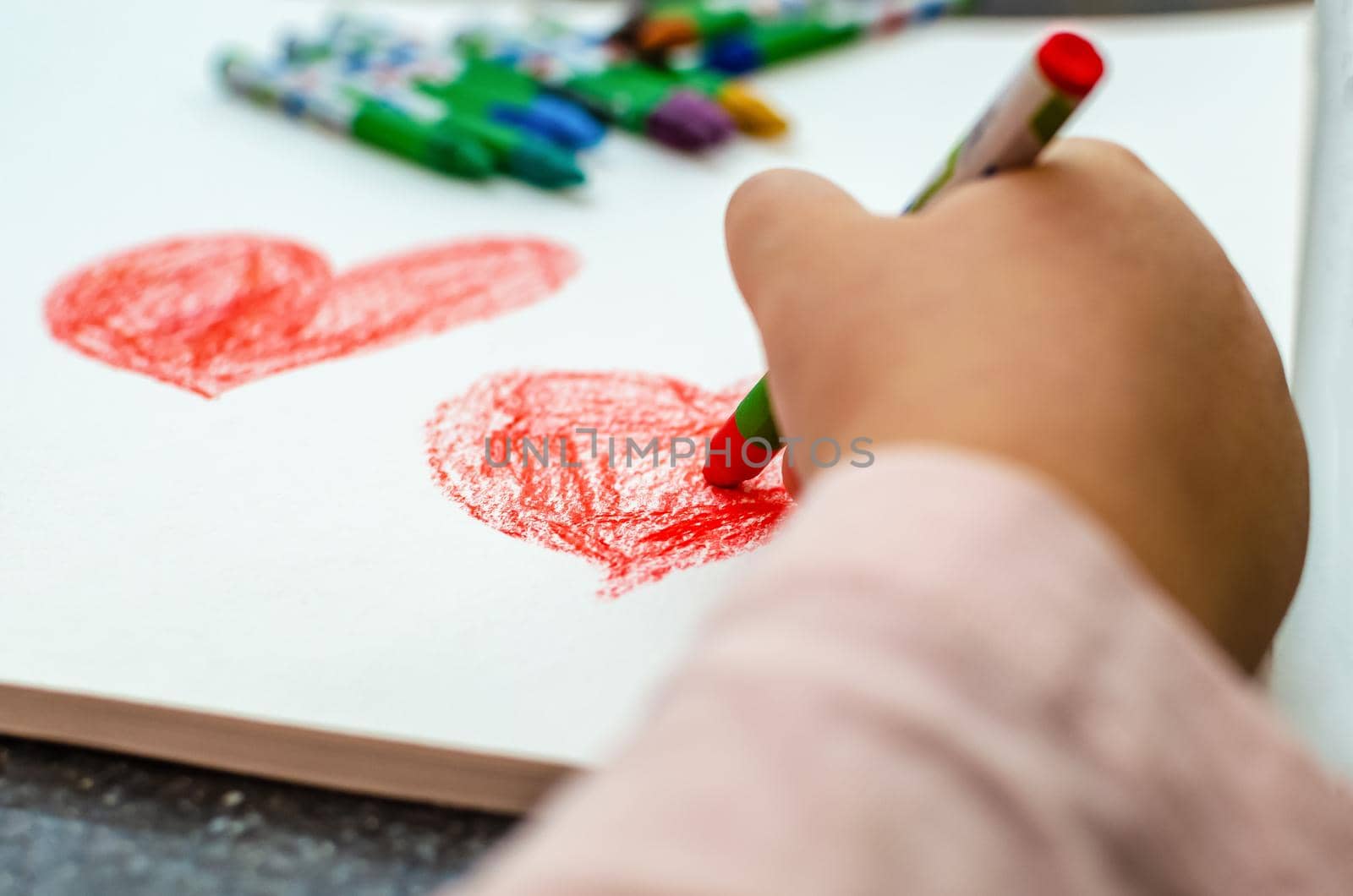 A little girl is drawing a heart with red chalk - high angle image with selective focus. Valentine's day concept.