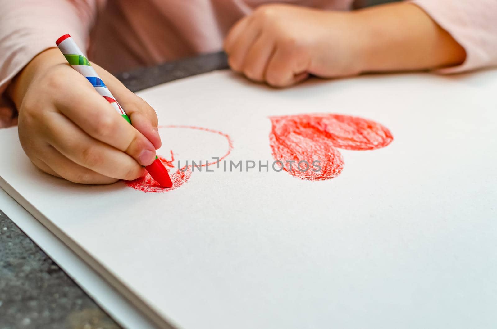 A little girl is drawing a heart with red chalk - high angle image with selective focus. Valentine's day concept.