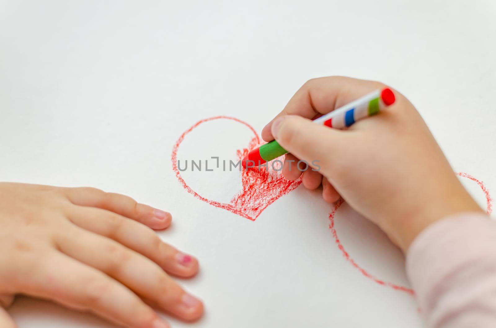 A little girl is drawing a heart with red chalk - high angle image with selective focus. Valentine's day concept.