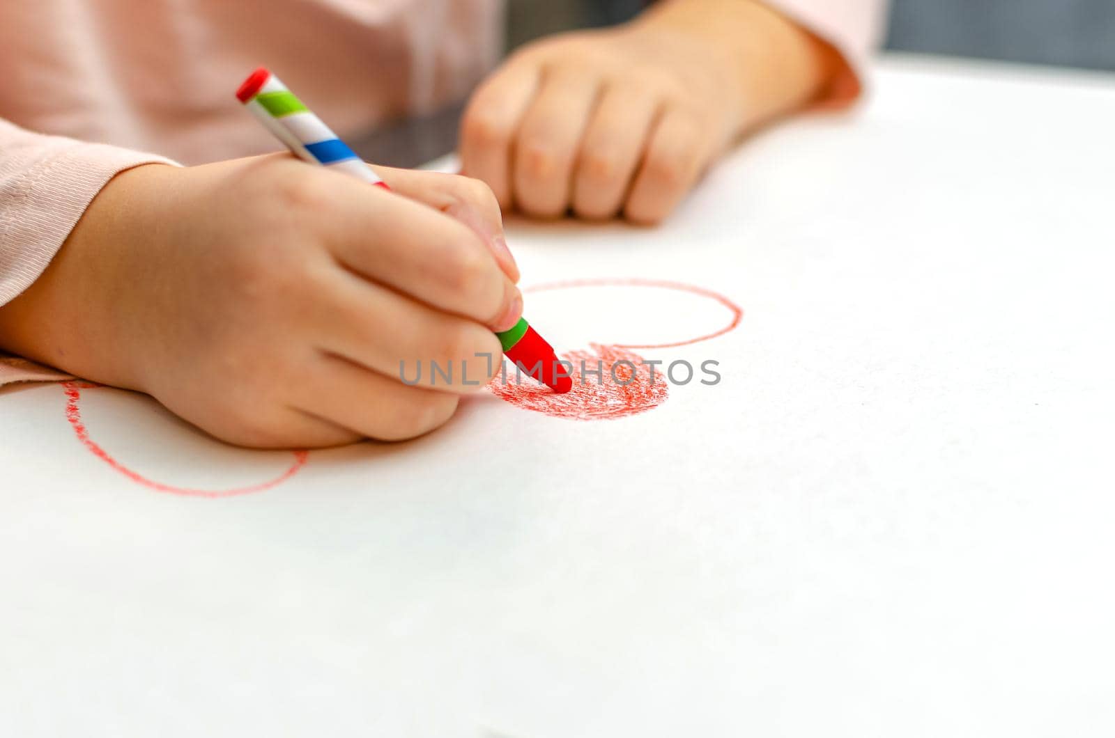 A little girl is drawing a heart with red chalk - high angle image with selective focus. Valentine's day concept.