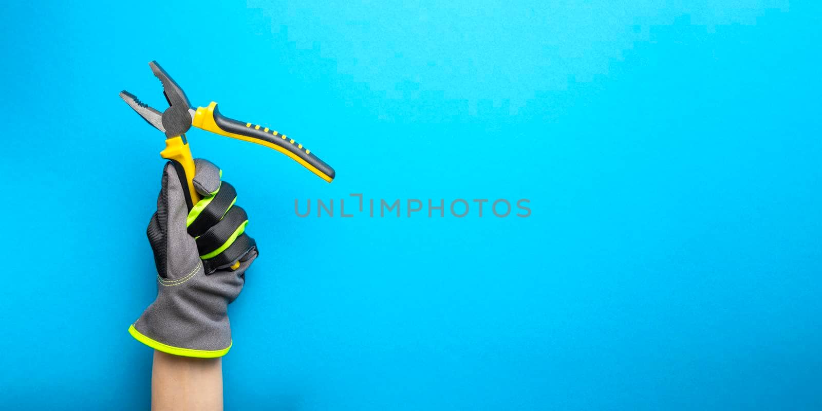 Pliers. Yellow and black pliers in the hand of an electrician on a blue monochrome background. Repair and installation tool. Banner for the design and printing of construction topics. by SERSOL