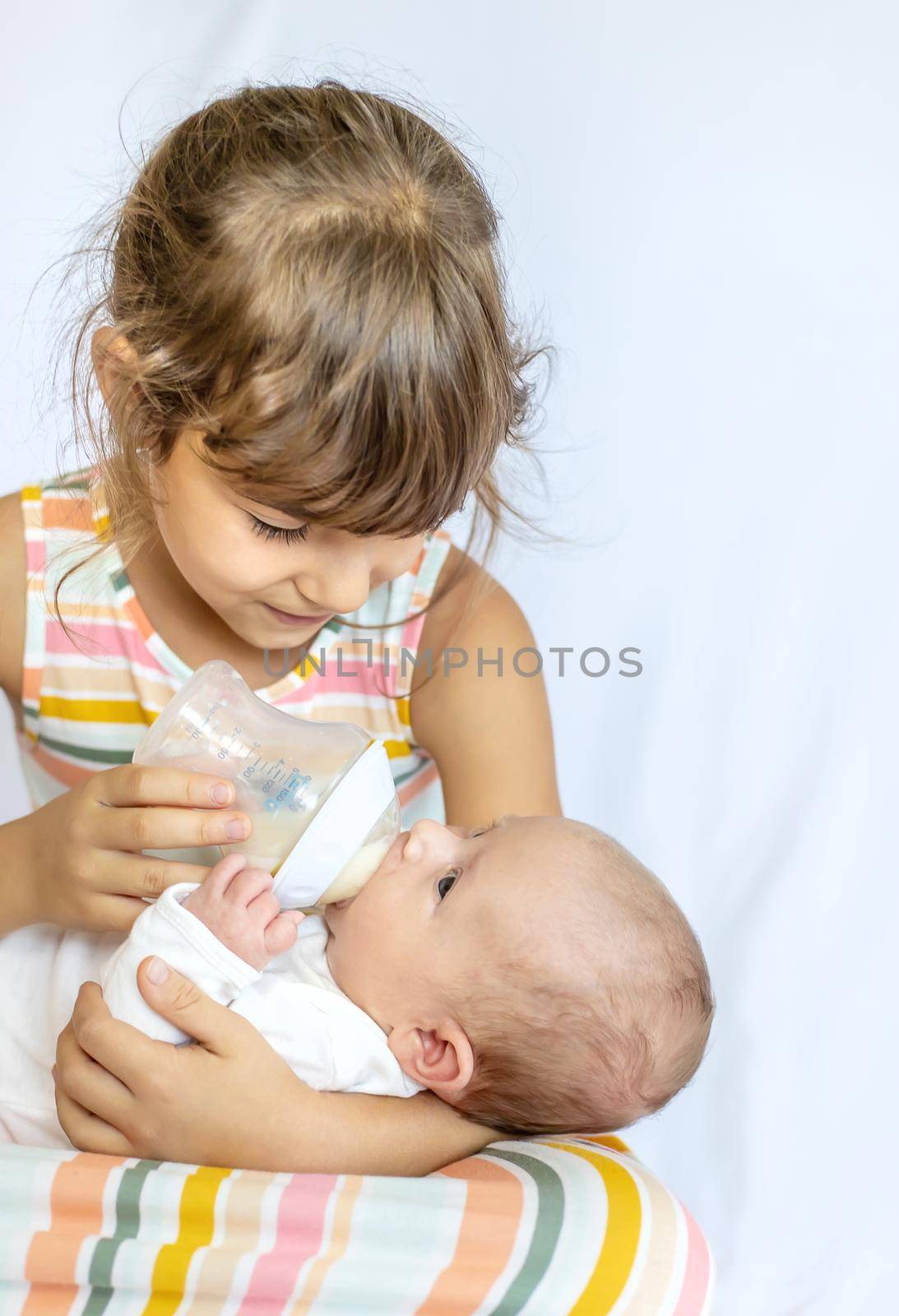 An older sister is feeding a newborn baby. Selective focus. People.