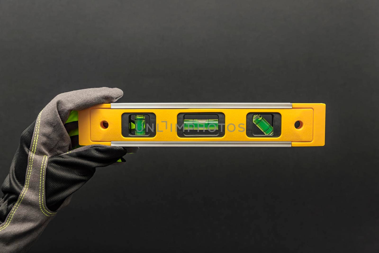Hand in gloves holds a yellow building level on a black background. Postcard or poster for print, place for text.