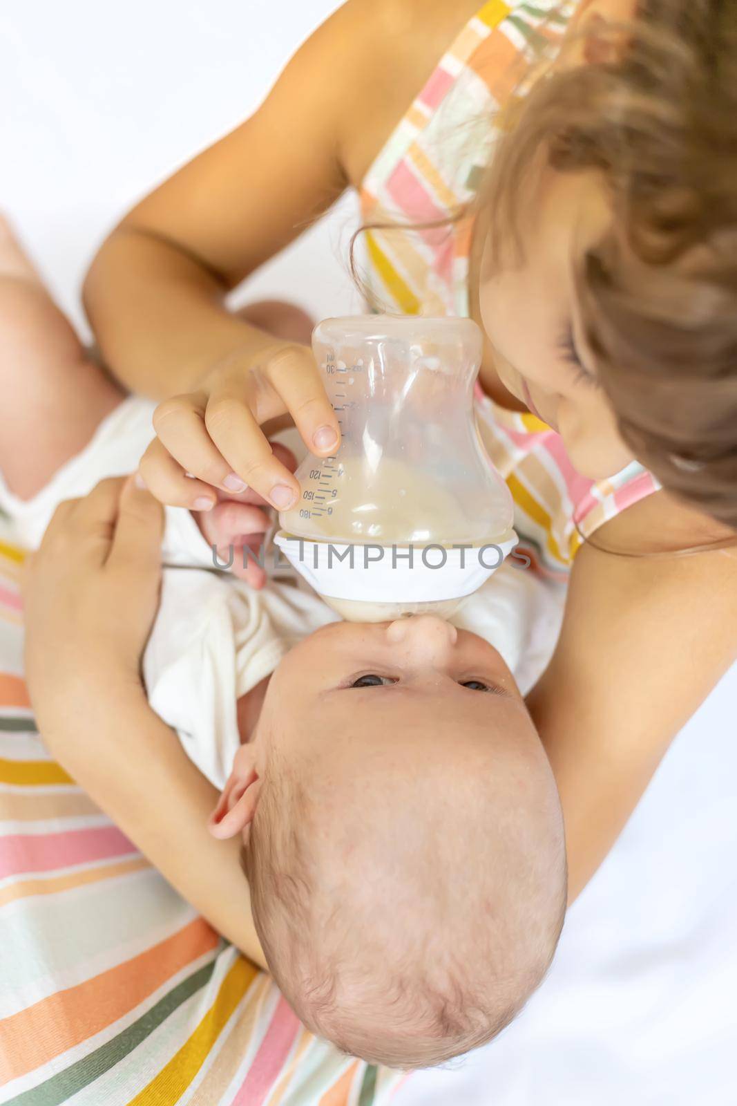 An older sister is feeding a newborn baby. Selective focus. by yanadjana