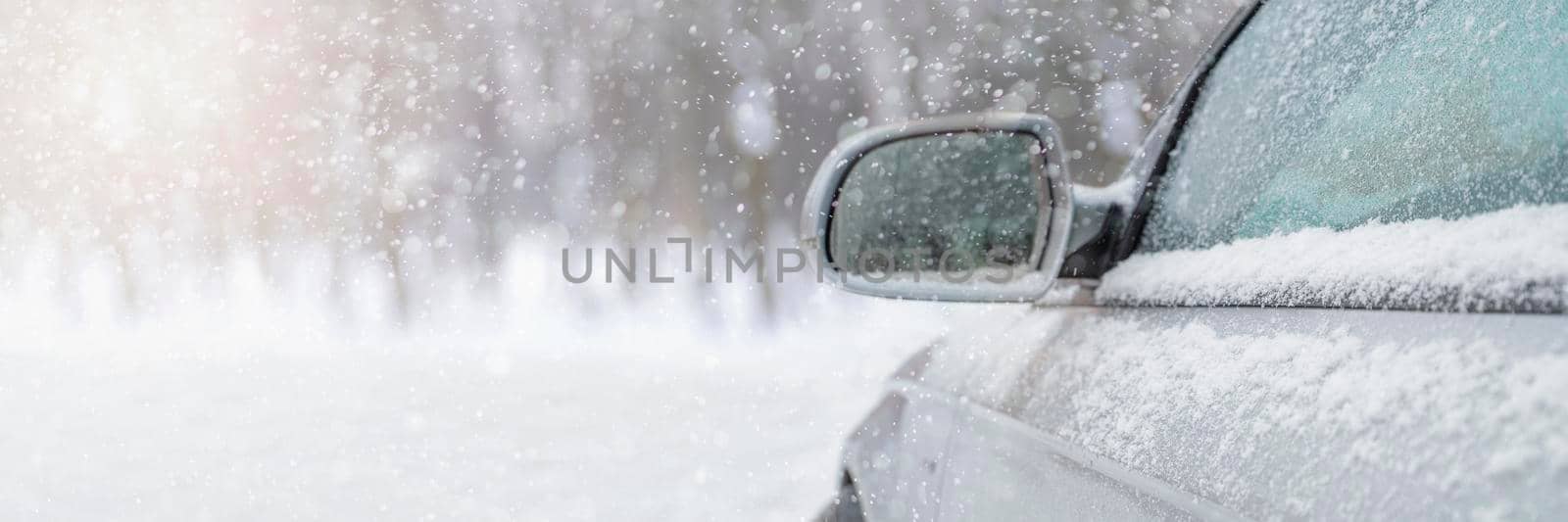 The car drives through the snow, the bright winter sun shines against the background of the forest. Close-up rearview mirror. The vehicle is covered with snow