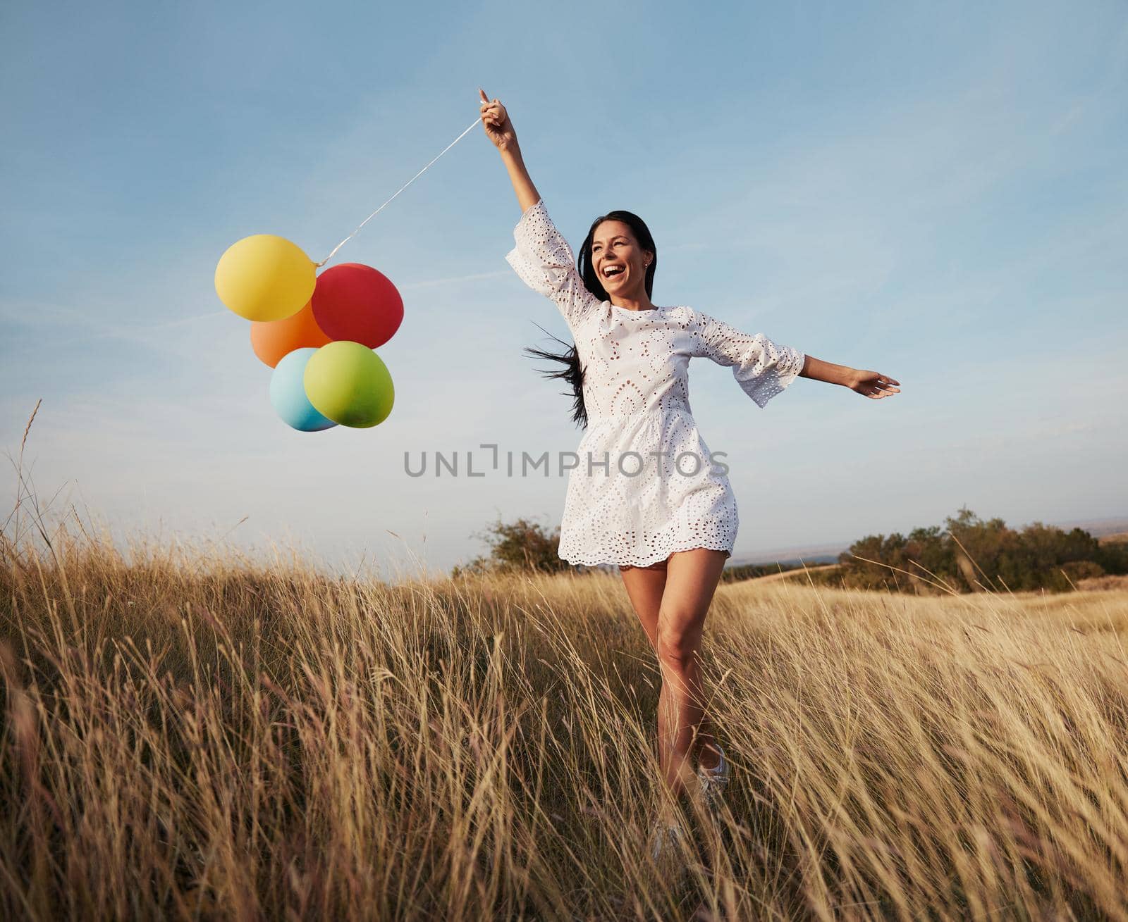 Happy young girl running with ballons through meadow grass