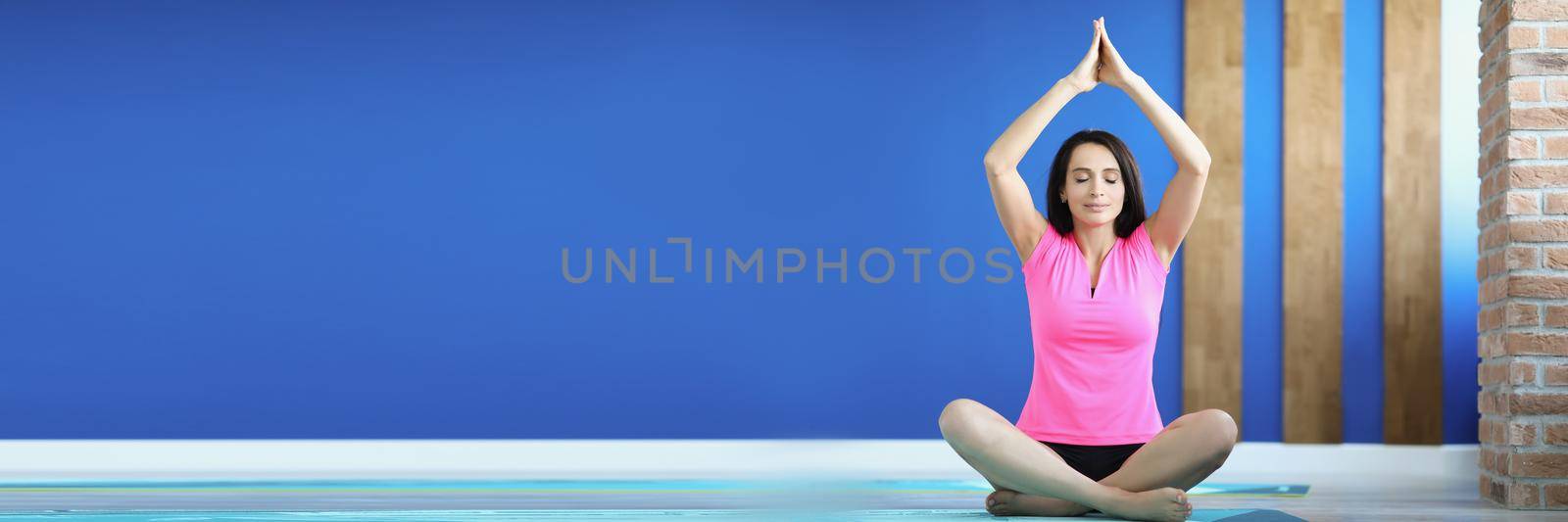 Portrait of young smiling woman practicing yoga position on mat in comfy outfit. Light studio for training and meditation. Healthcare, wellness, peace of mind concept