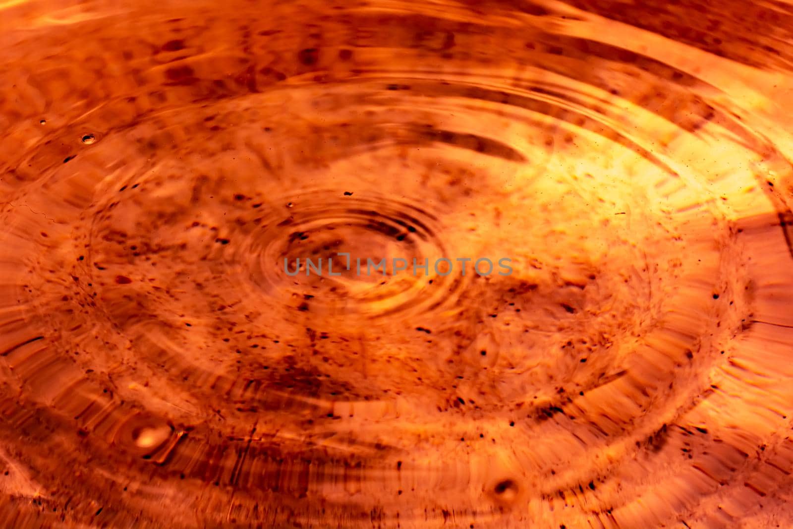 Circles and small ripples on orange-brown liquid. Backdrop