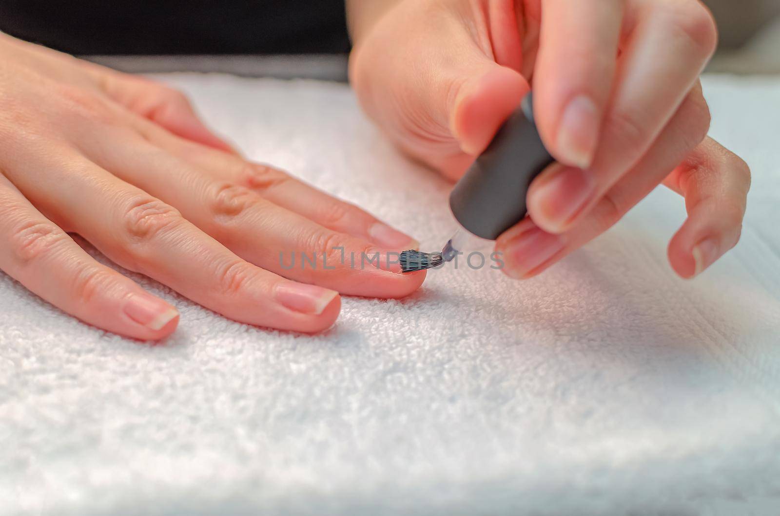 A woman applies a primer to her nails before applying varnish. Close-up of a hand