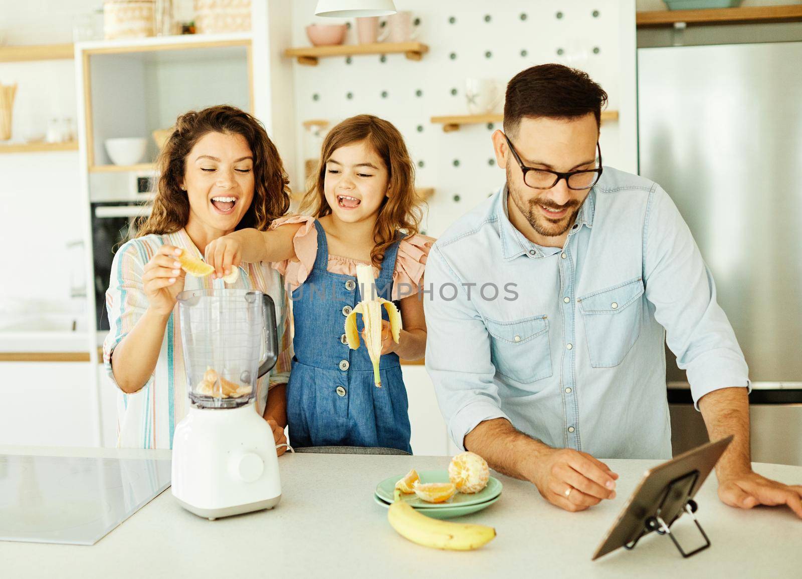 Family preparing smoothie juice in blender and having fun in the kitchen at home