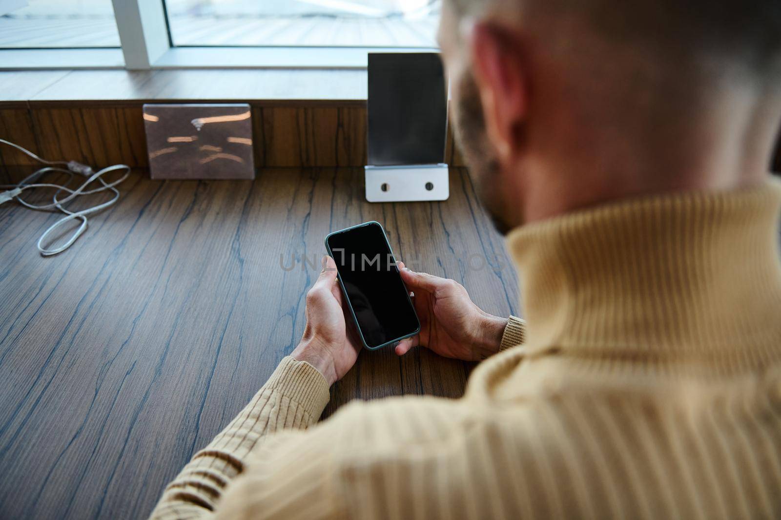 Focus on smartphone with black blank screen with copy space for ads and mobile applications in the hands of a man browsing websites on internet waiting to board a flight in airport departure terminal