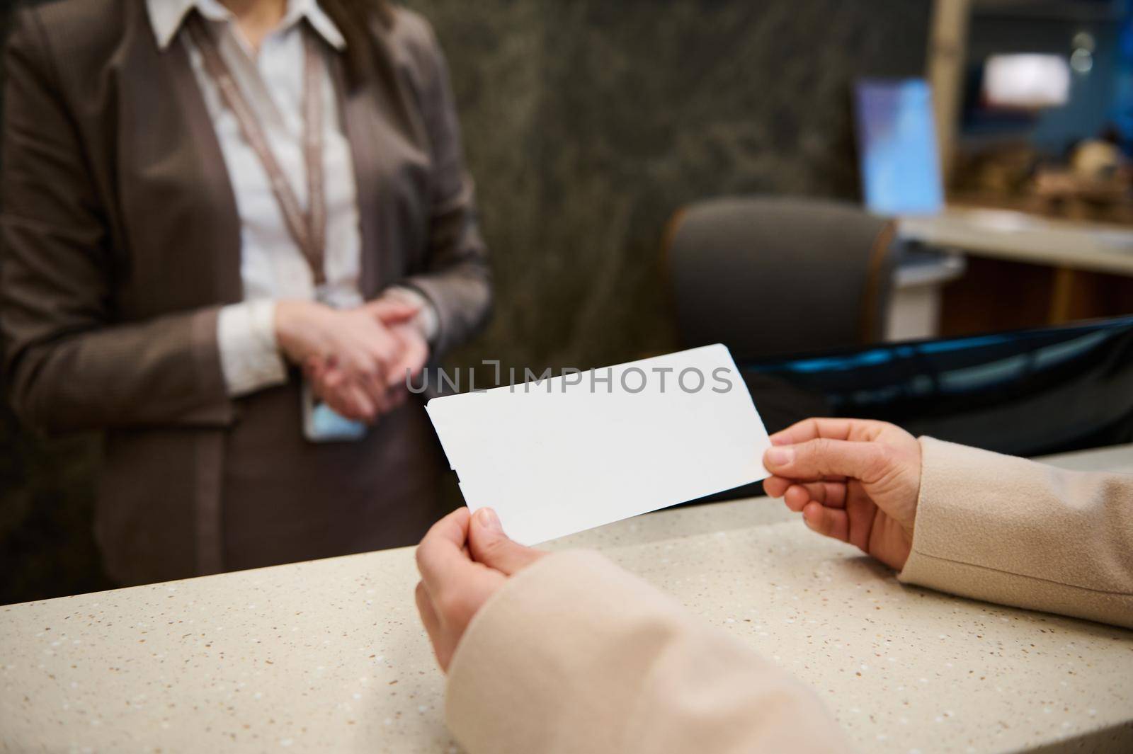 Focus on a white blank ticket with copy space for advertising text in the hands of unrecognizable woman standing by check-in counter in the VIP lounge of the international airport departure terminal
