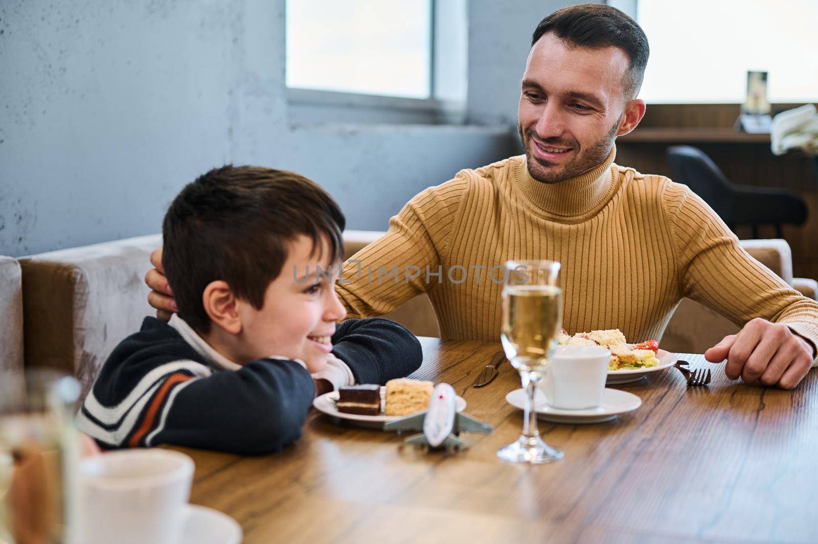 Handsome young man of Middle-Eastern ethnicity, dad, father stroking son's head while enjoying a healthy meal together in a restaurant