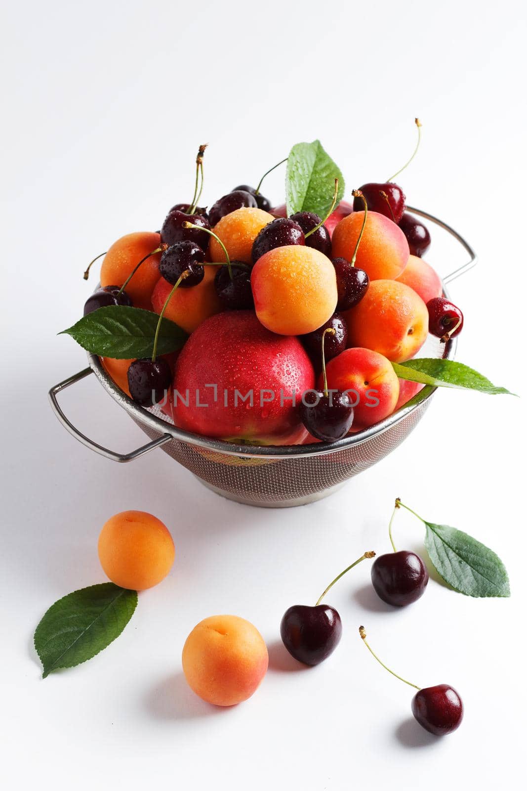 apricots and cherries in a metal bowl on a white background.