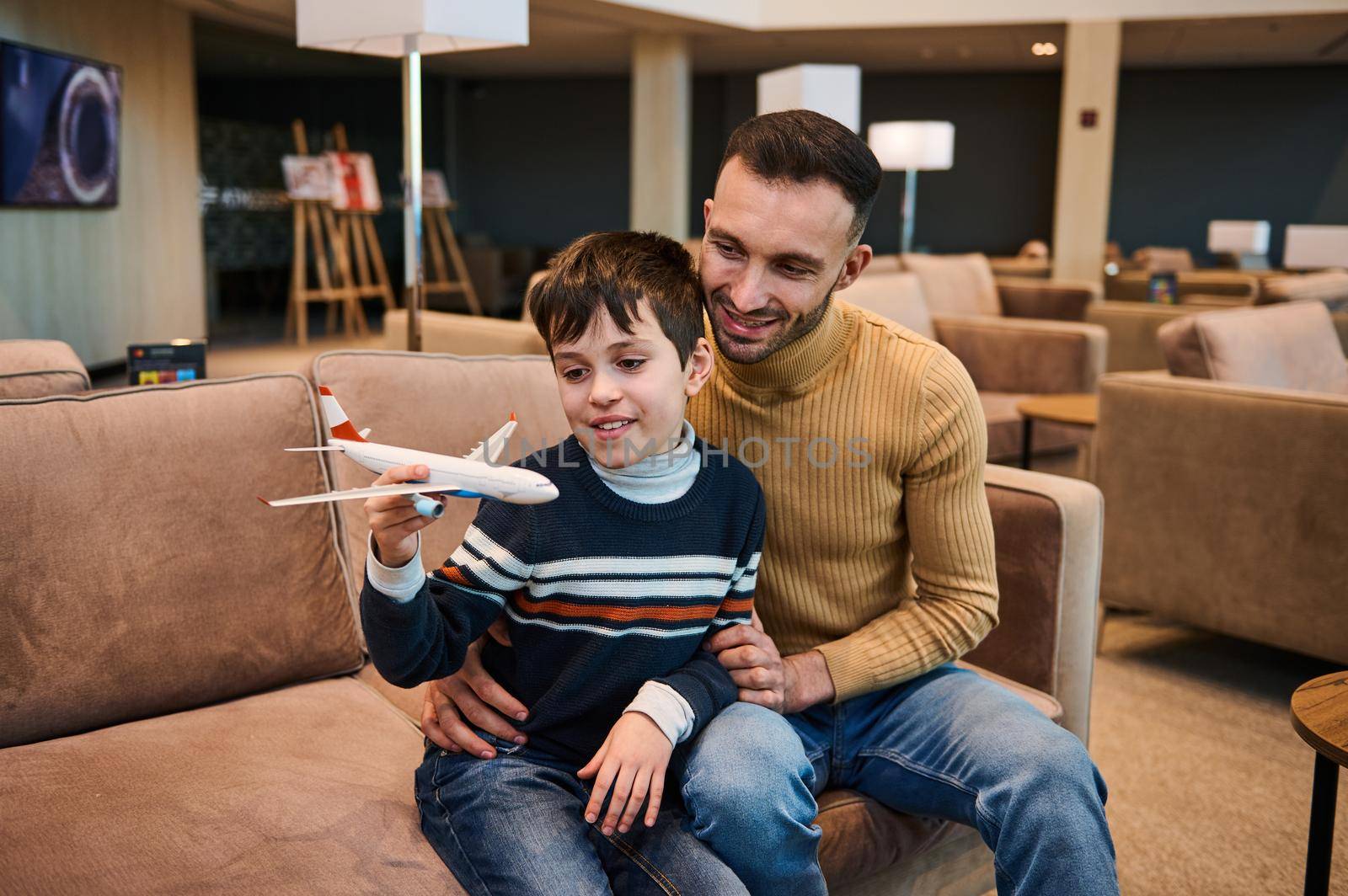 Handsome Caucasian young man playing toy plane with his adorable younger brother in VIP lounge at international airport departure terminal while waiting to board flight during family travel