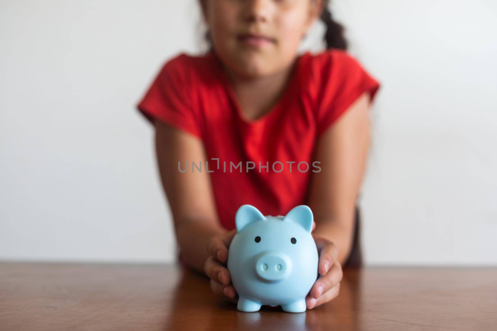 Smiling little girl posing with a piggy bank in her hands, standing against a blue background in a studio with free space. Family savings by Andelov13