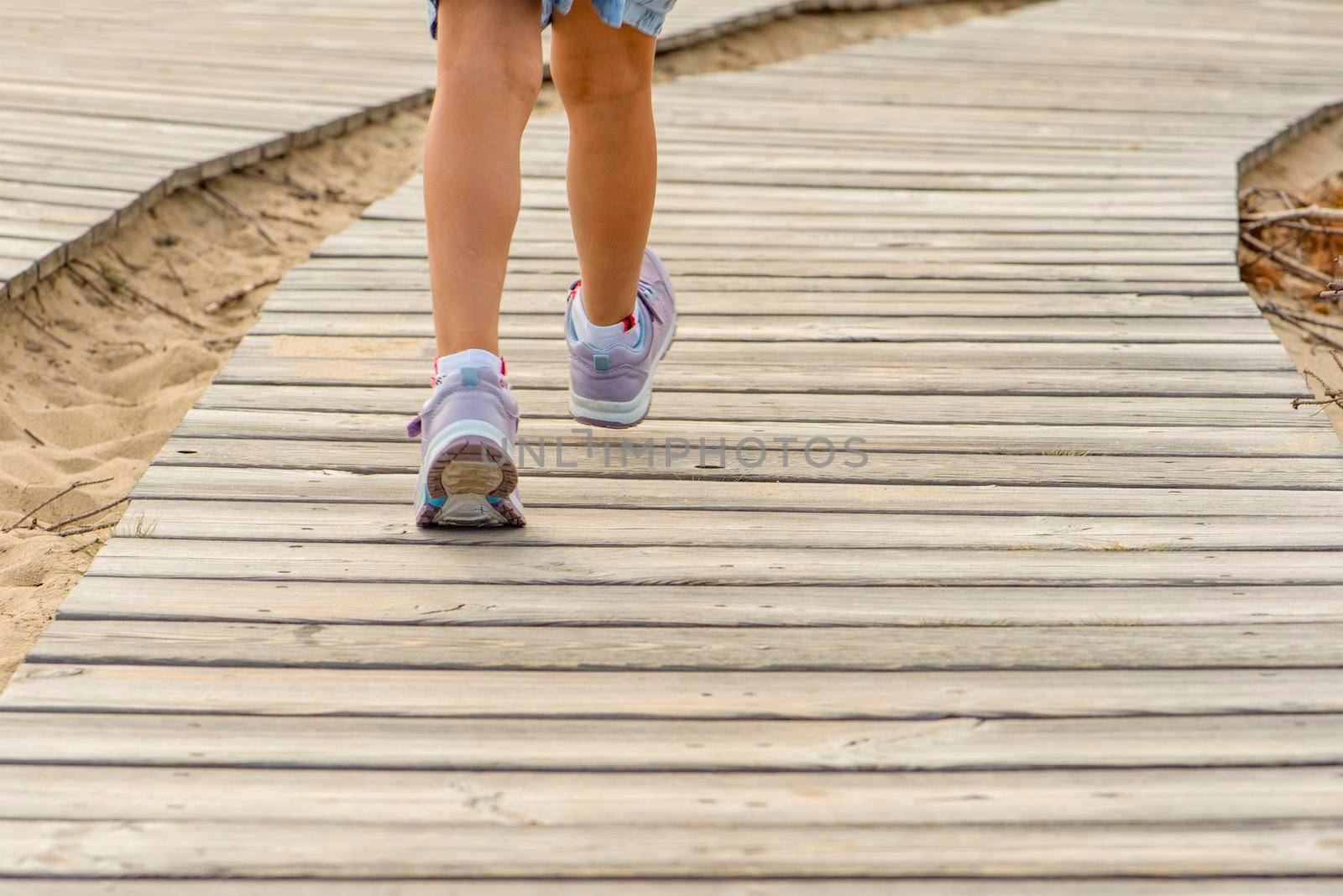 Wooden path in the mountains. Wooden flooring. Winding tourist path made of boards in the mountains. Close-up girl's legs go to the mountains along the tourist route.