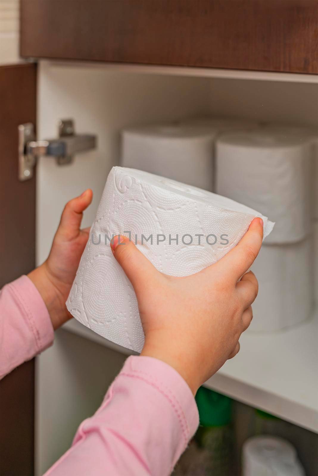 Toilet paper, roll of toilet paper in hand. Stocks of toilet paper. Girl puts toilet paper in the cabinet. Vertical photo by SERSOL