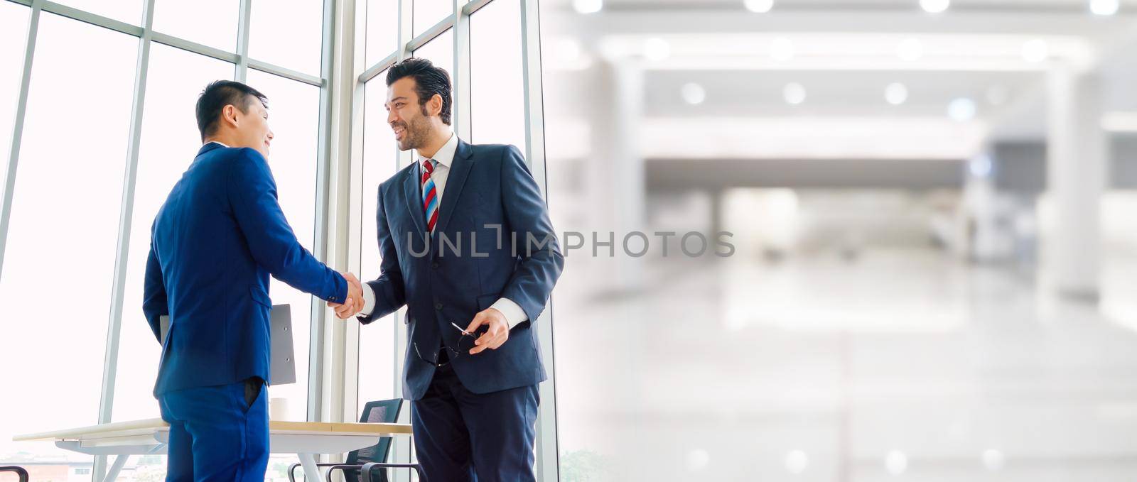 Business people handshake in corporate office in widen view showing professional agreement on a financial deal contract.