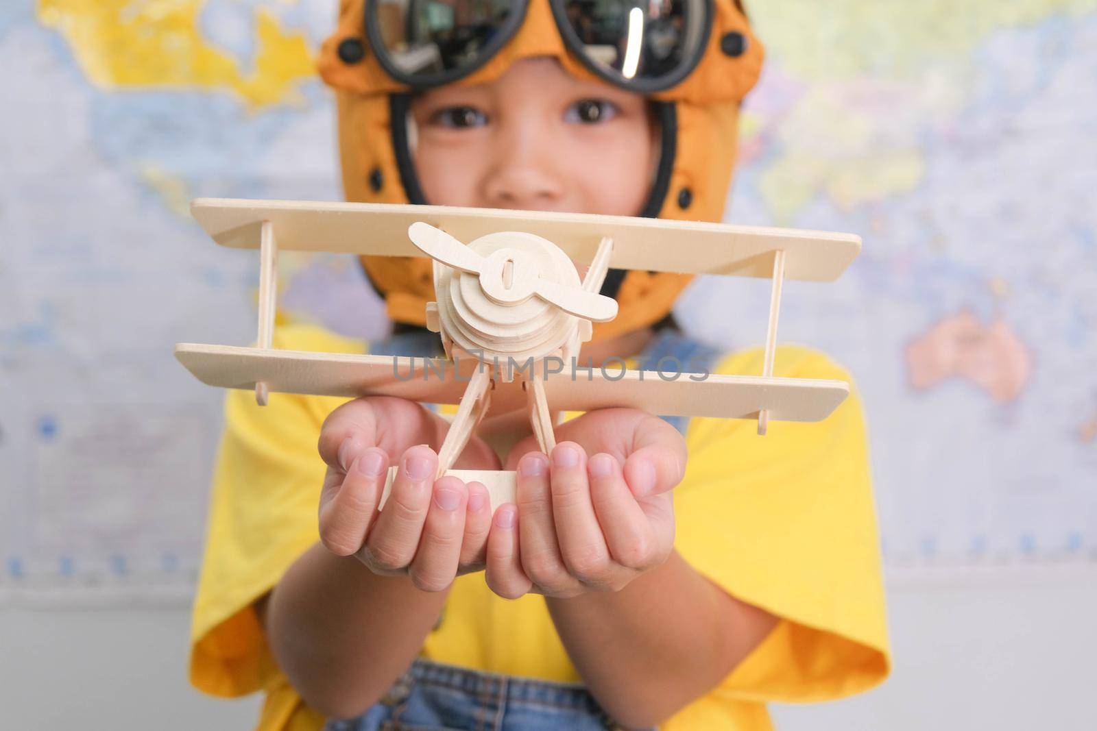 Little girl in a pilot hat holding a toy plane in her hands having fun in kids room at home. Happy child girl at home dreaming of travel and tourism. Childhood dream imagination and Travel concepts. by TEERASAK