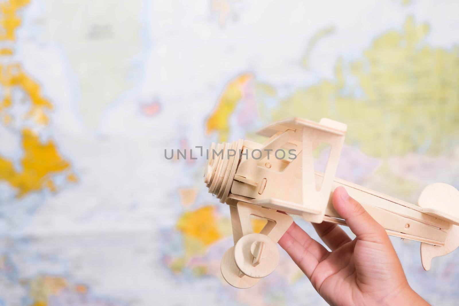 Close-up of wooden toy plane in children's hands on world map background in kids room at home. Childhood dream imagination and Travel concepts.