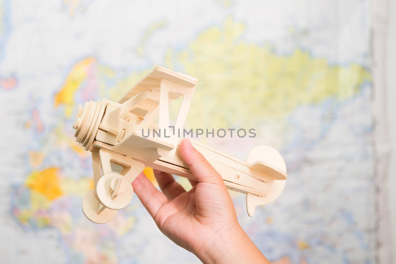 Close-up of wooden toy plane in children's hands on world map background in kids room at home. Childhood dream imagination and Travel concepts.