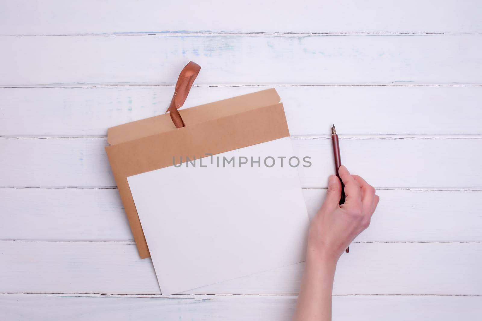 One Craft envelop, white paper and ink pencil in hand on white wooden background