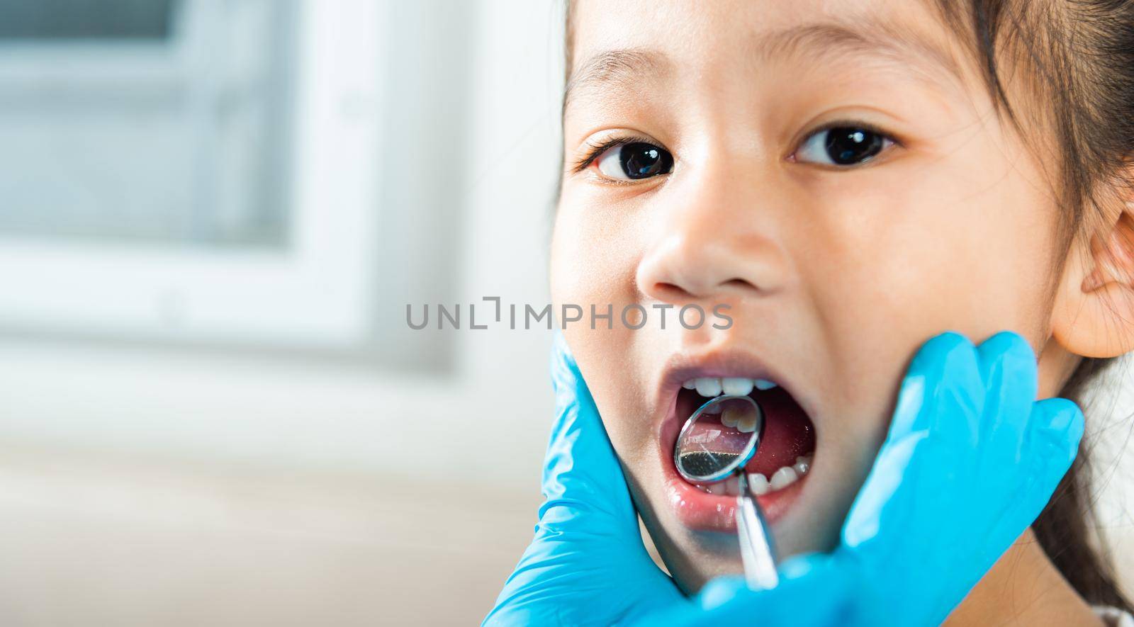 Doctor examines oral cavity of little child uses mouth mirror to checking teeth cavity by Sorapop