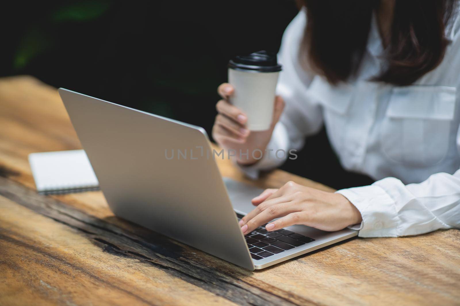 closeup hand of business woman working on laptop and holding cup hot coffee on wooden table with a cup of coffee. Business concept work form home anywhere.