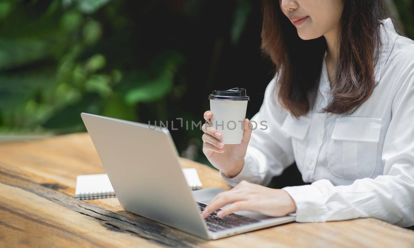 Business woman working on laptop and holding cup hot coffee on wooden table with a cup of coffee. Business concept work form home anywhere. by Wmpix