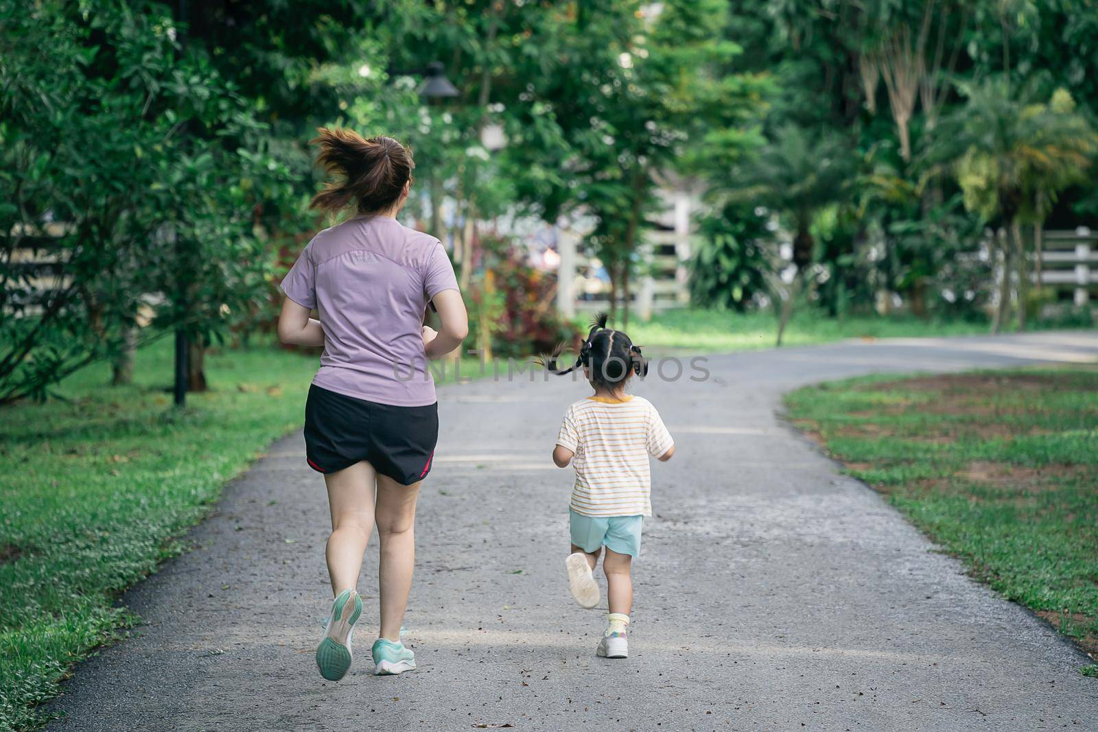 Mother and daughter runners are jogging in the park. Evening. Family activities . Mother and son in sportswear are running and having fun. by Wmpix