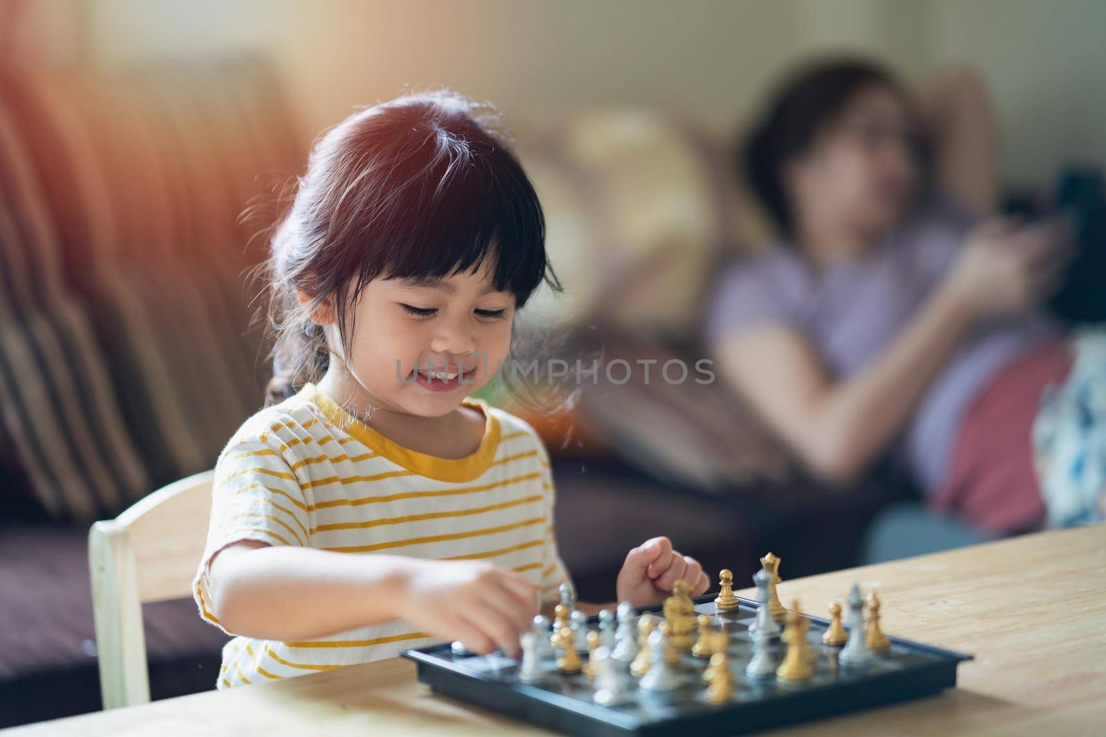 Little asian baby playing chess in the living room at home.Smart kid.fashion children. Little genius Child. Intelligent game.Chessboard. Baby activity concept. by Wmpix