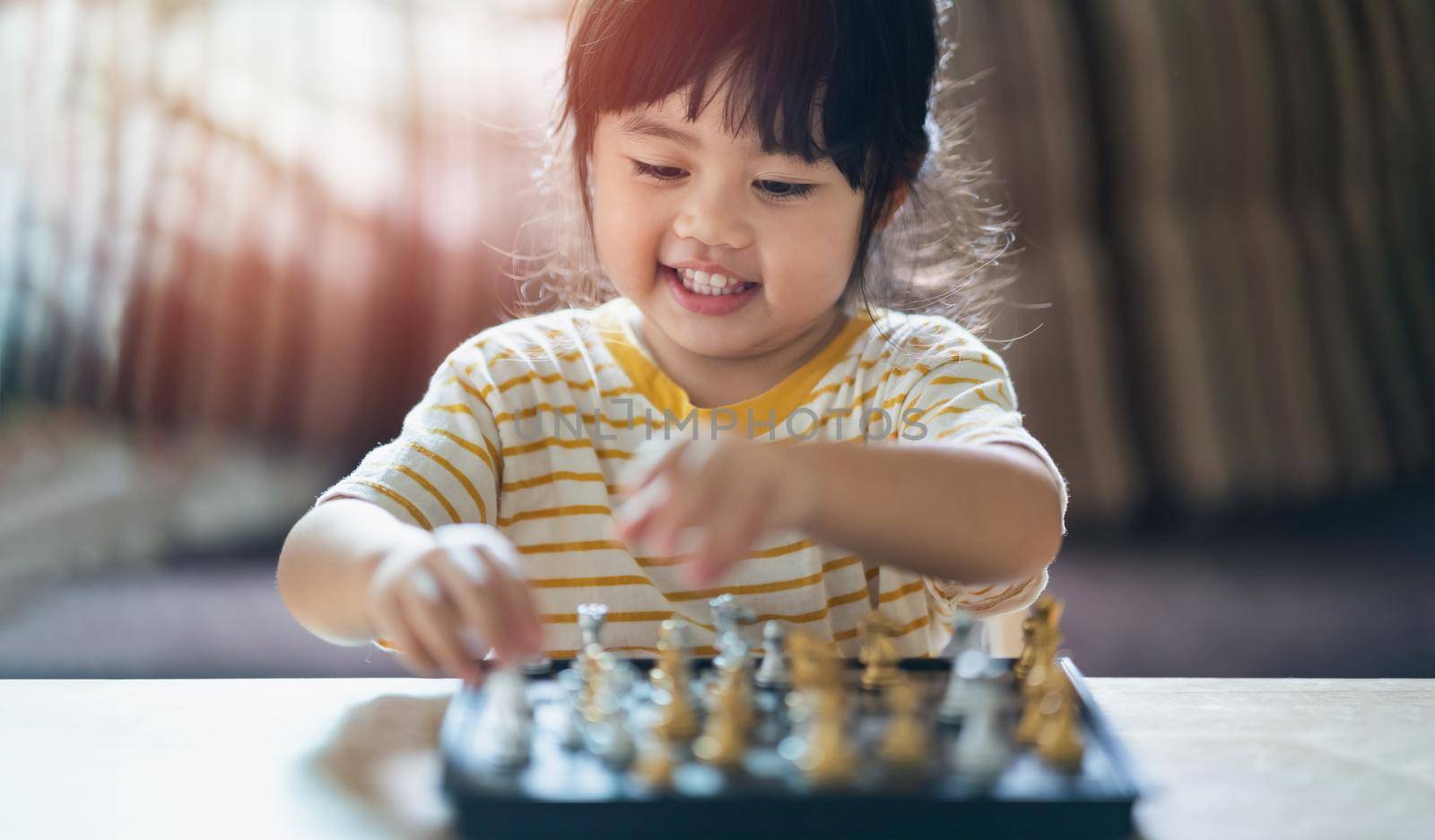 Little asian baby playing chess in the living room at home.Smart kid.fashion children. Little genius Child. Intelligent game.Chessboard. Baby activity concept. by Wmpix