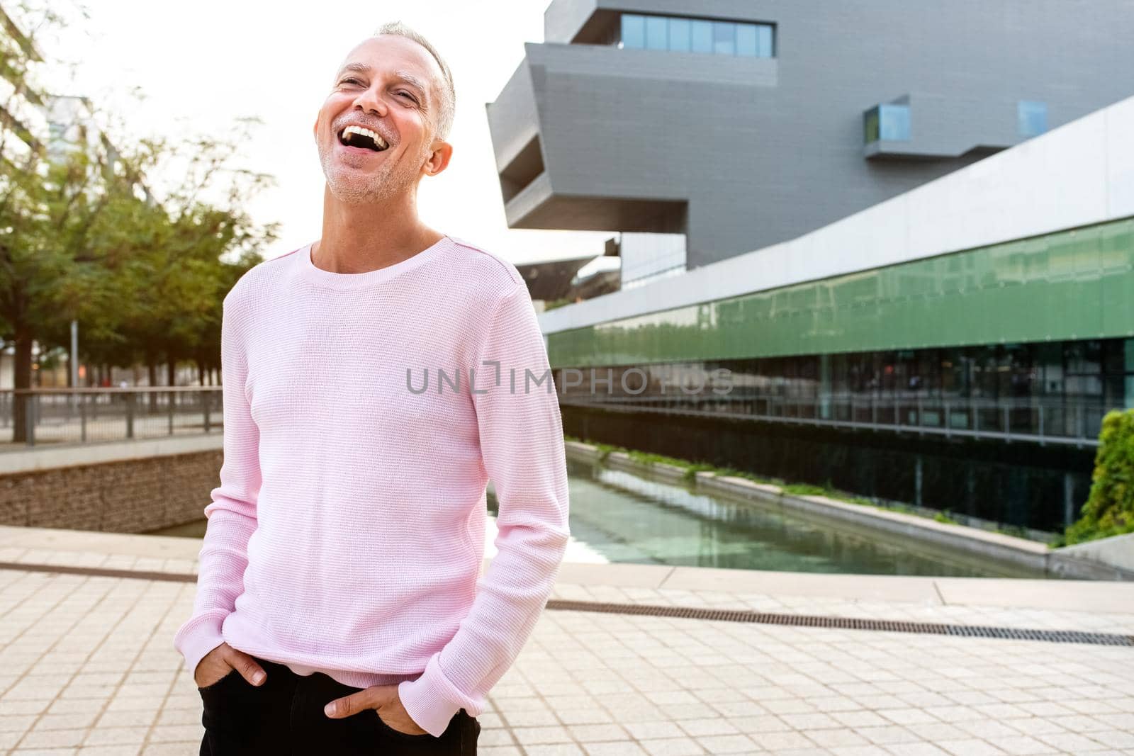 Portrait of caucasian man wearing pink sweater laughing on the street. Copy space. by Hoverstock