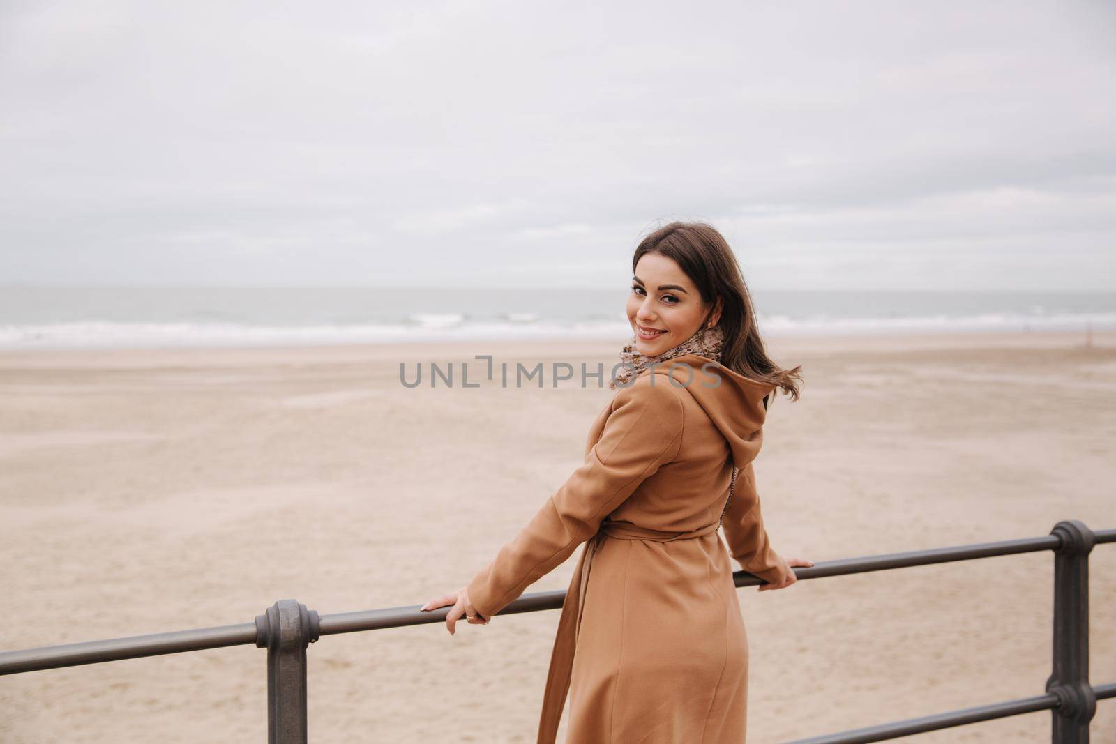 Stylish lady with make up in beautiful coat standing along North Sea. Woman smile by Gritsiv