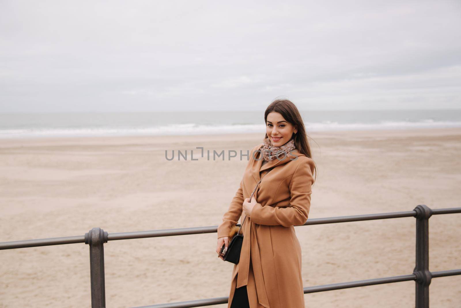 Stylish lady with make up in beautiful coat standing along North Sea. Woman smile.