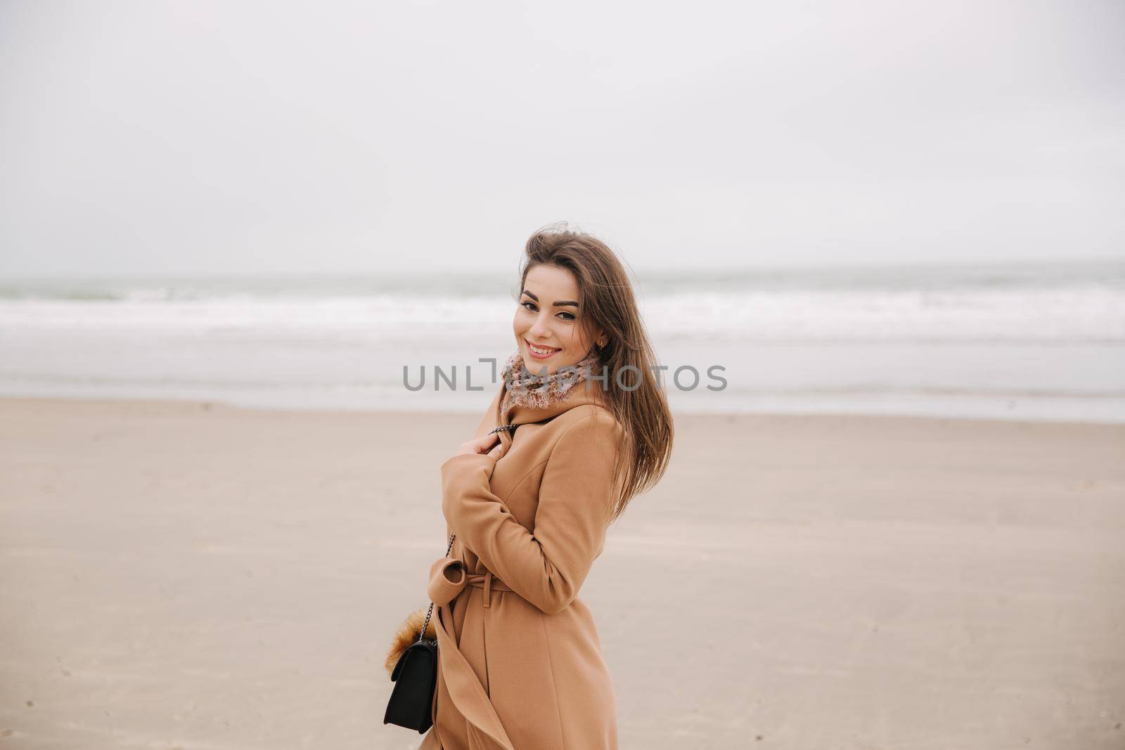 Portrait of beautiful woman walkink along the coast near the north sea. Elegant lady in brown coat with fashion make up stand in front of the sea.