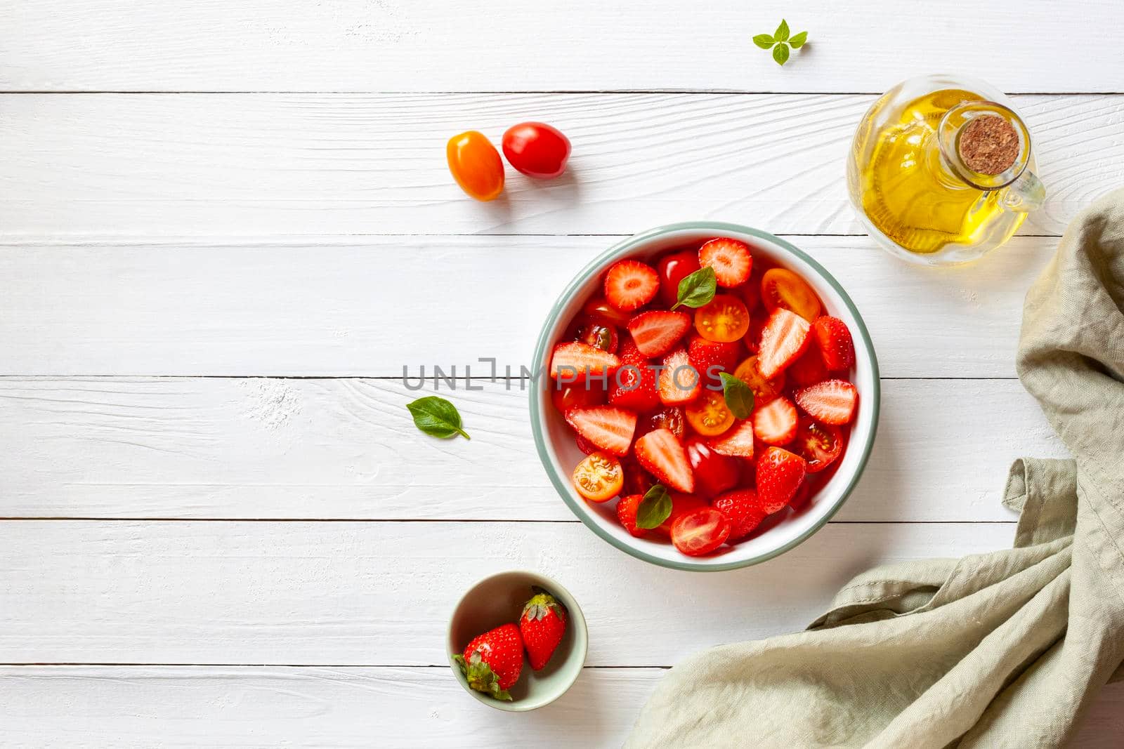 tomato cherry and strawberry salad decorated with basil leaves, white wooden background, top view, copy space