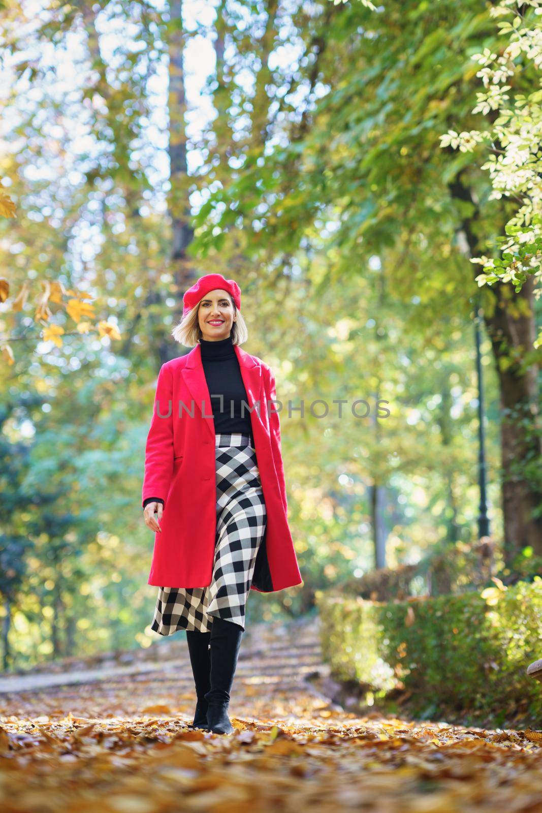 Cheerful woman in coat walking in park by javiindy
