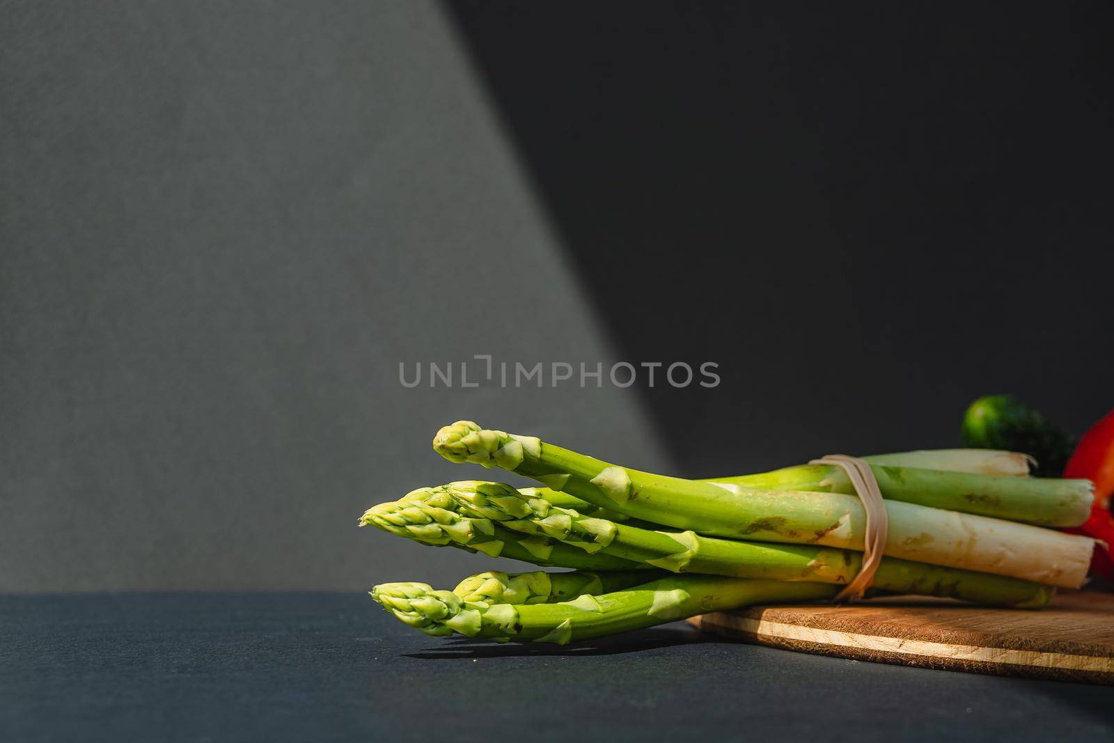 branches of fresh green asparagus on a wooden board, dark gray background, top view. Basic trend concept with copy space