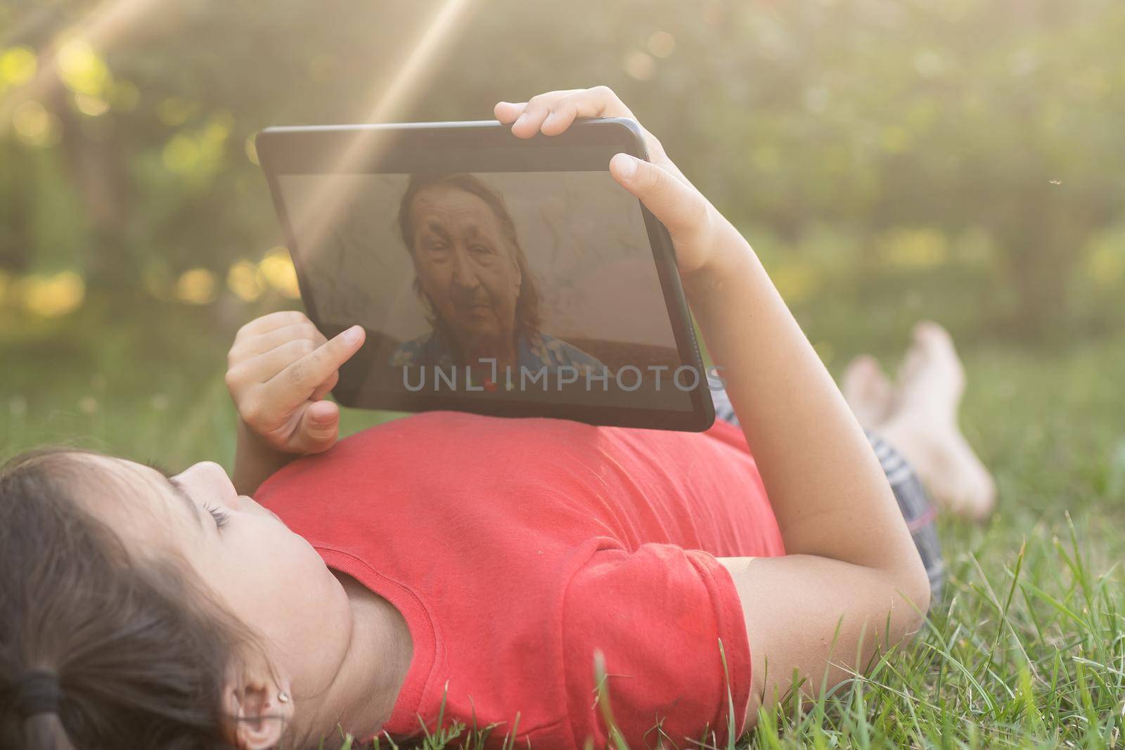 Girl on the grass with a tablet chat in her hands in the garden.