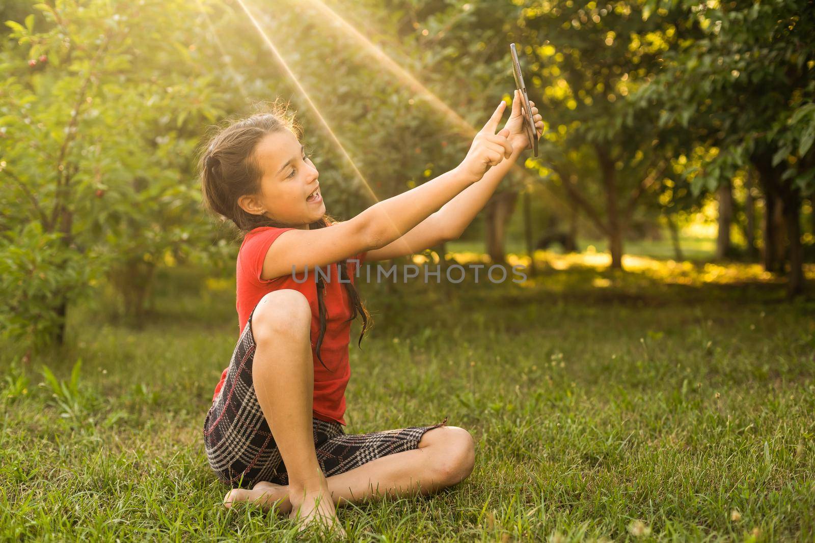 Girl on the grass with a tablet chat in her hands in the garden by Andelov13