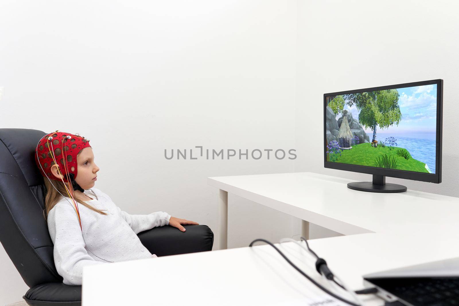 Girl wearing headgear looking to a screen while sitting on a chair during a biofeedback therapy