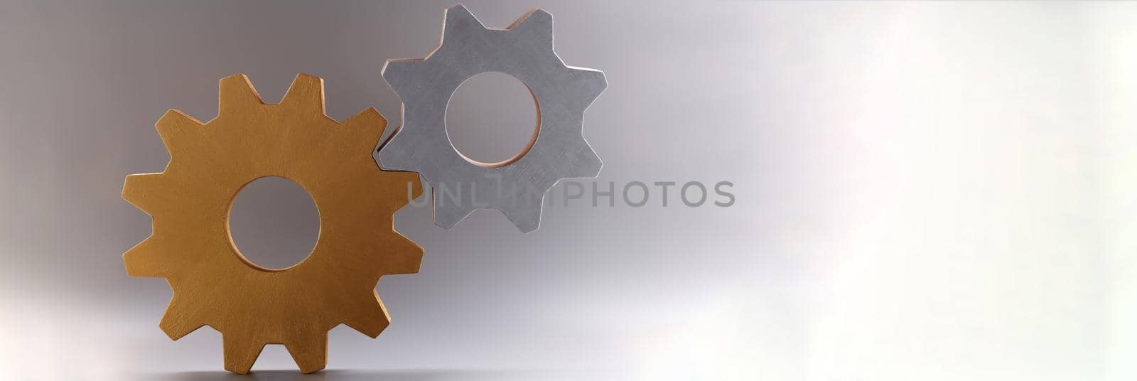 Closeup of golden and silver connected gears on gray background. Teamwork concept