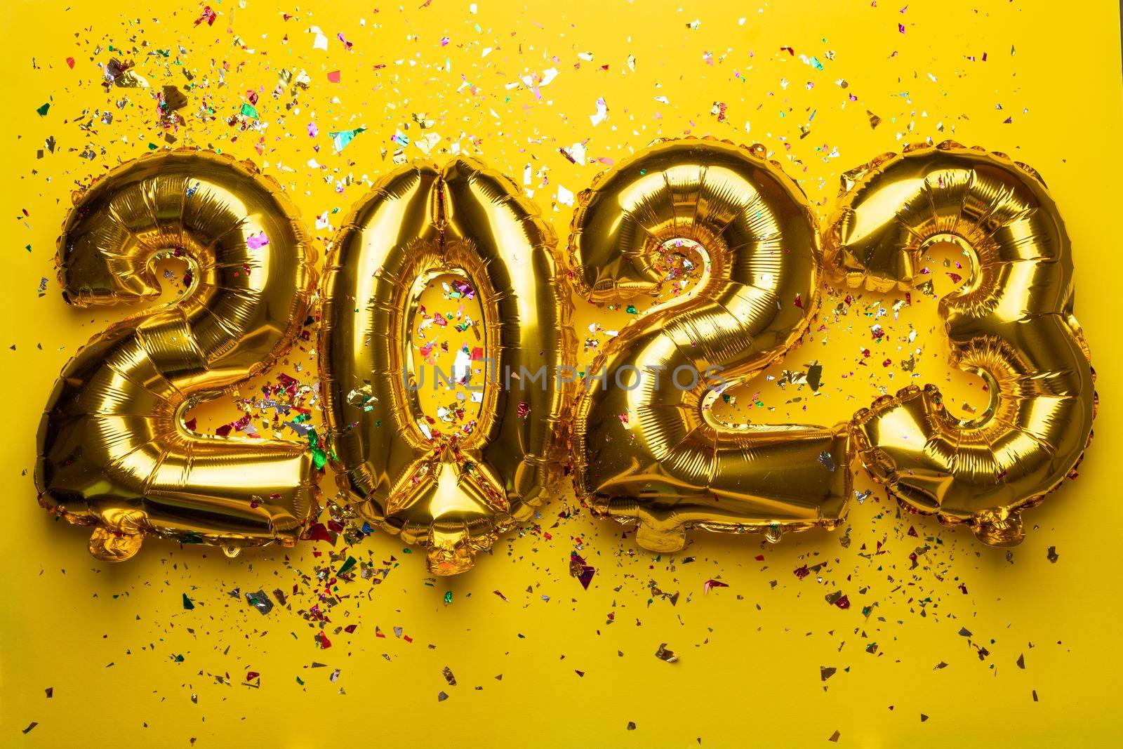 2023 concept Happy New Year from golden foil balloon and confetti on yellow background