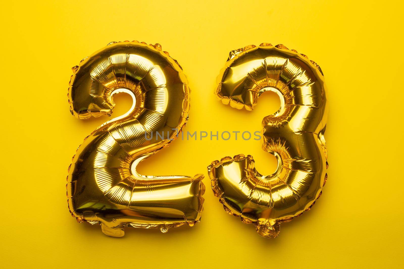 Happy New Year concept. Number 23 from golden foil balloon on yellow background