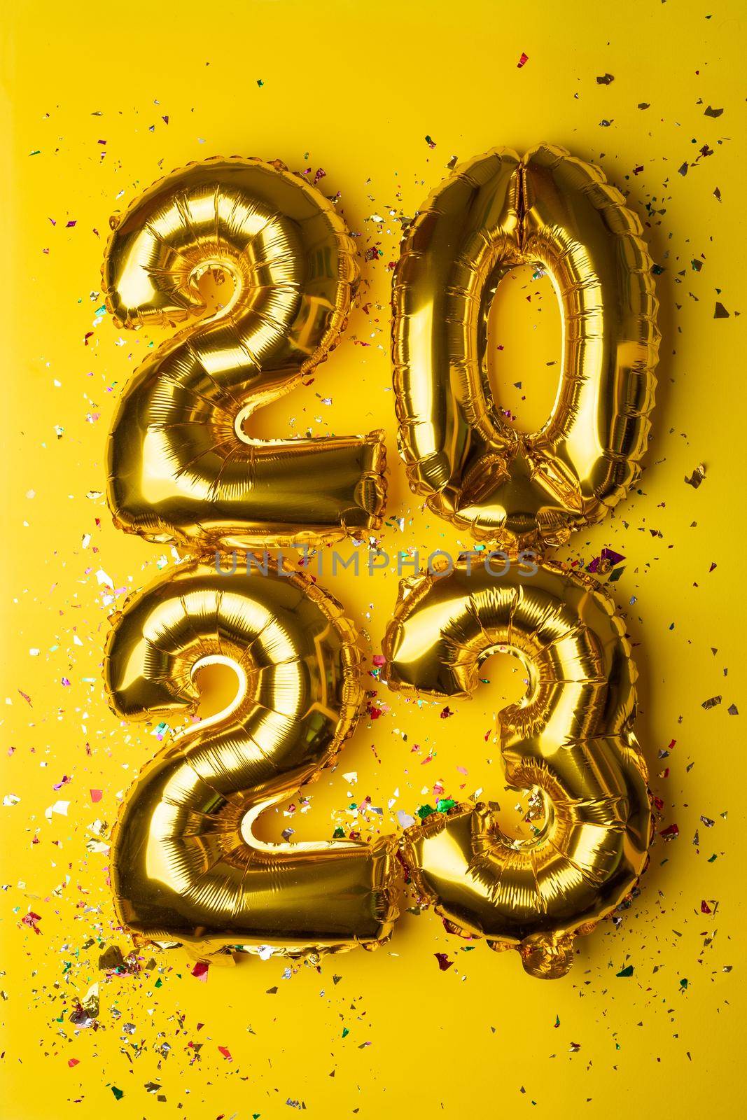 2023 concept Happy New Year from golden foil balloon and confetti on yellow background by adamr