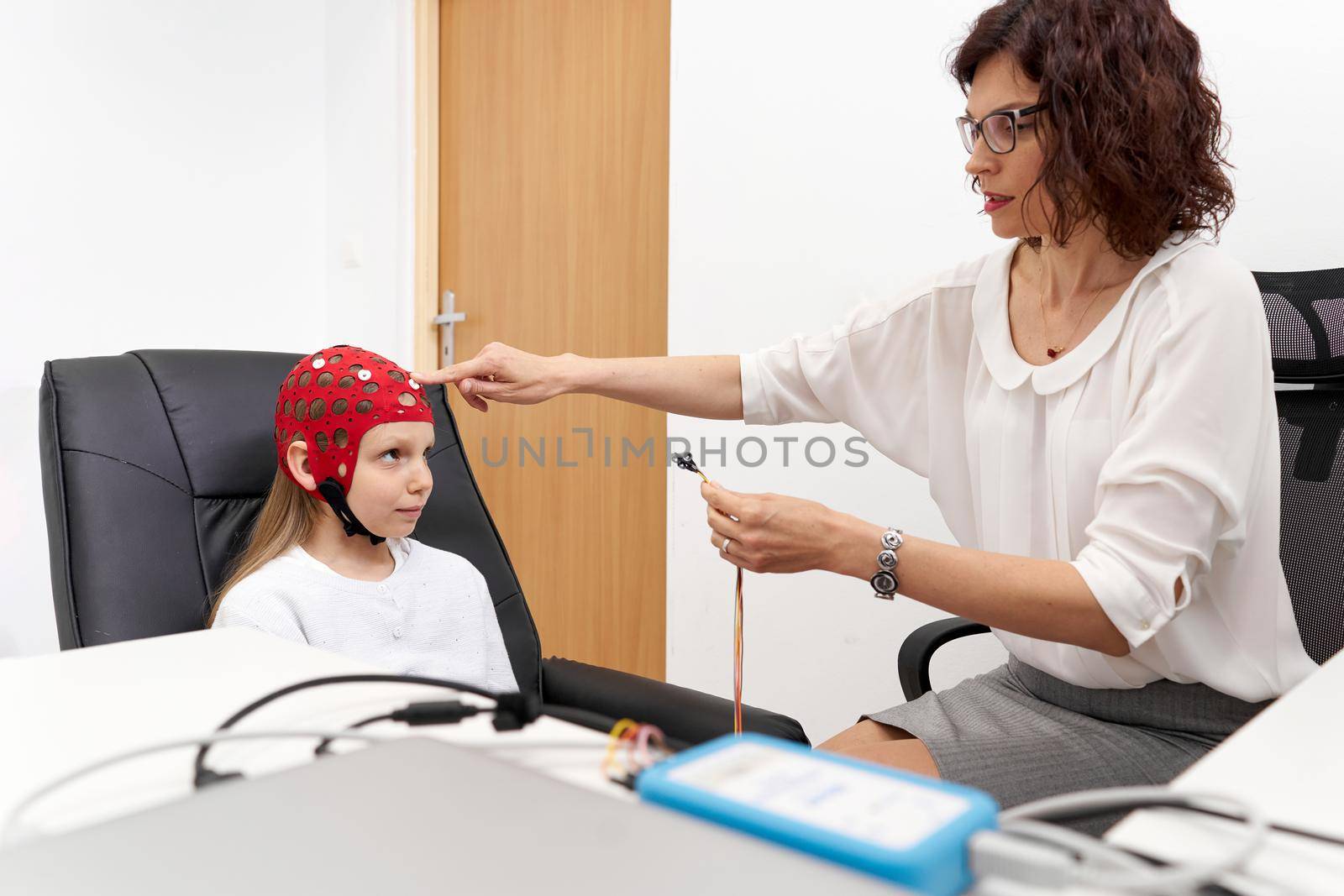 Female doctor putting electrodes on a girl sitting on a chair in a biofeedback session