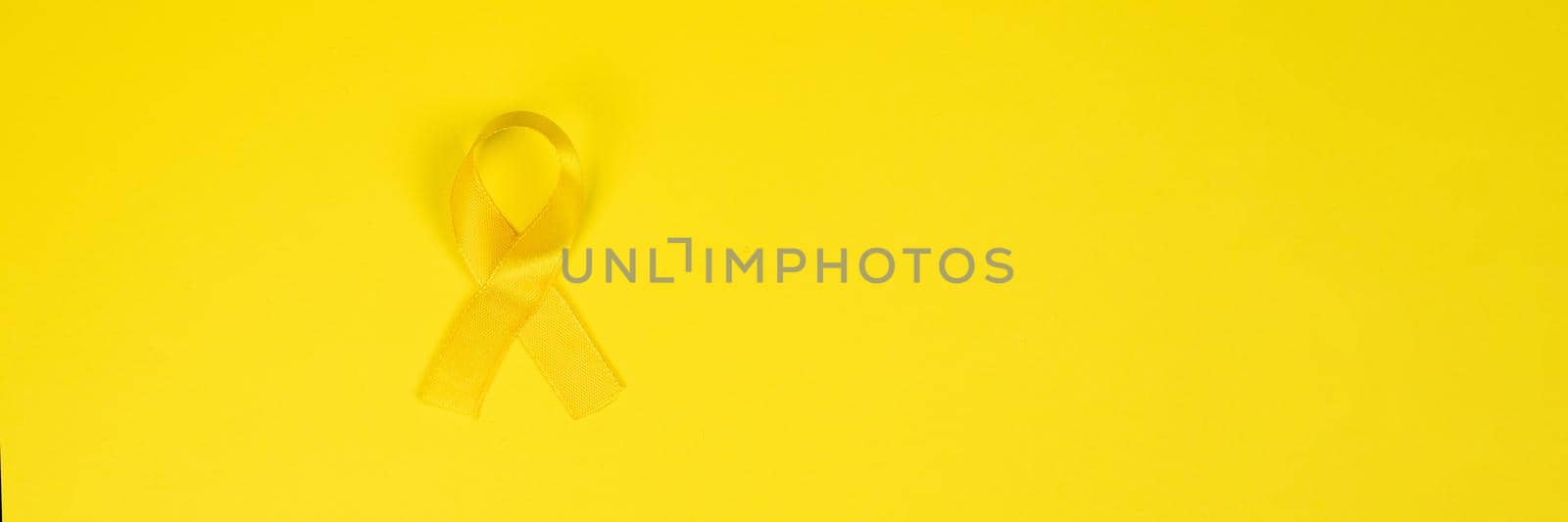 Yellow gold ribbon on a yellow background. Children cancer concept. Awareness month. Childhood Cancer Day February, 15. Web banner.